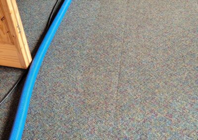 Hye-Vac carpet cleaning hose and equipment cleaning a carpeted room inside a wood-paneled office.