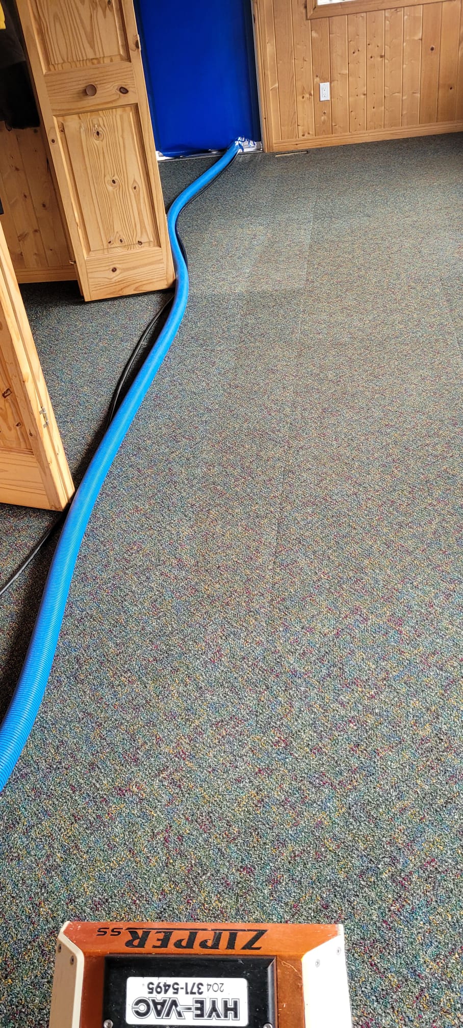 Hye-Vac carpet cleaning hose and equipment cleaning a carpeted room inside a wood-paneled office.